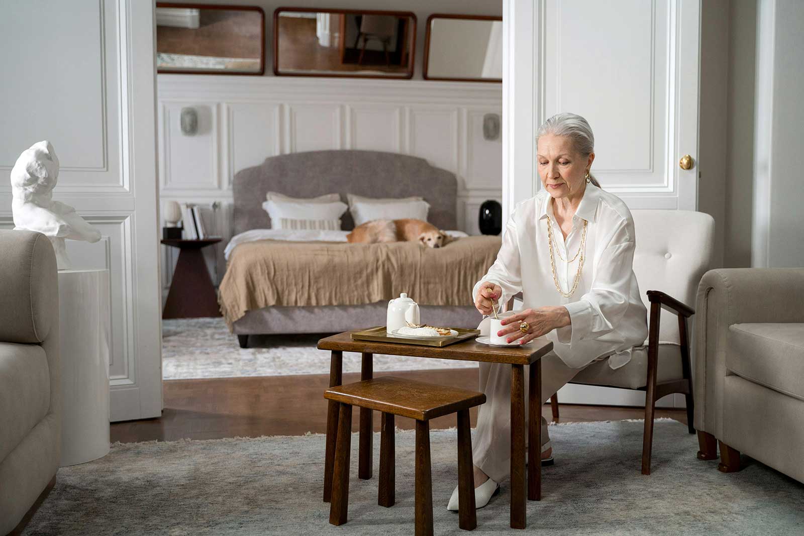 An older woman enjoying a warm drink in a cozy, comfortable living room, representing the peace of mind and predictable heating costs achieved in 2026.